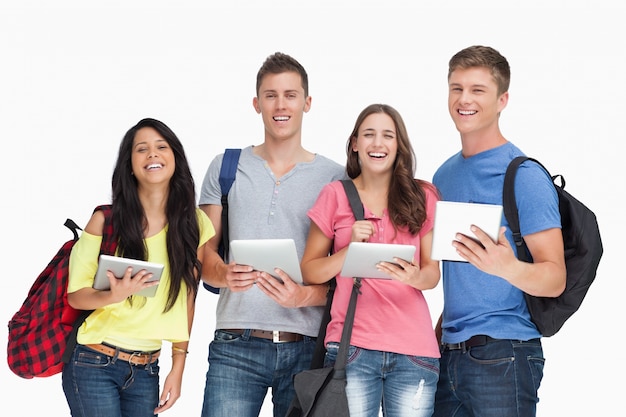 Un grupo de estudiantes con tabletas y mochilas sonriendo y mirando a la cámara