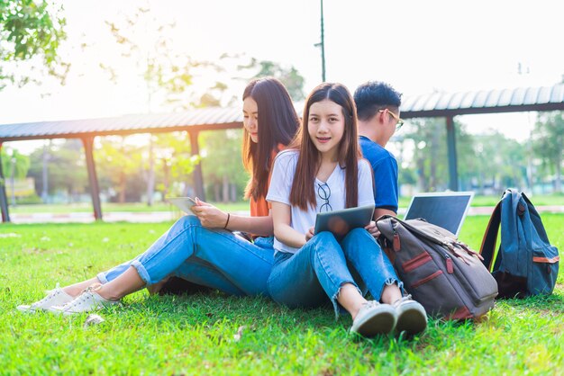 Grupo de estudiantes universitarios asiáticos usando tableta y computadora portátil en campo de hierba en el exterior