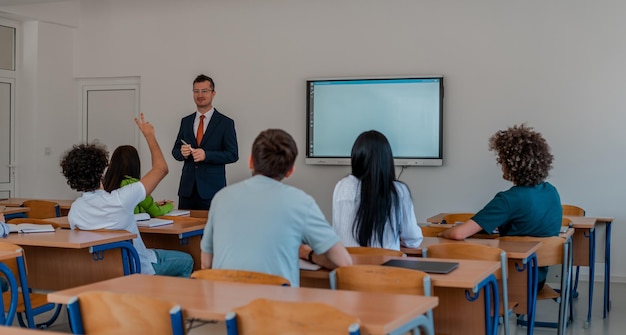 En el grupo de estudiantes universitarios que escuchan a un profesor universitario y participan en discusiones y debates, el estudiante levanta la mano con una pregunta para el profesor.