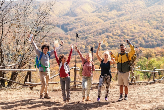 Grupo de excursionistas con las manos en alto y mirando a cámara. Longitud total, tiempo de otoño.