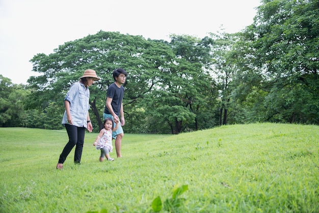 Foto grupo de familia asiática con niños pequeños caminando por el campo de hierba verde en el parque en verano.