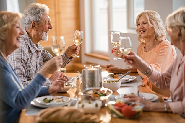 Grupo de felices amigos mayores divirtiéndose mientras brindan con vino durante el almuerzo en la mesa del comedor