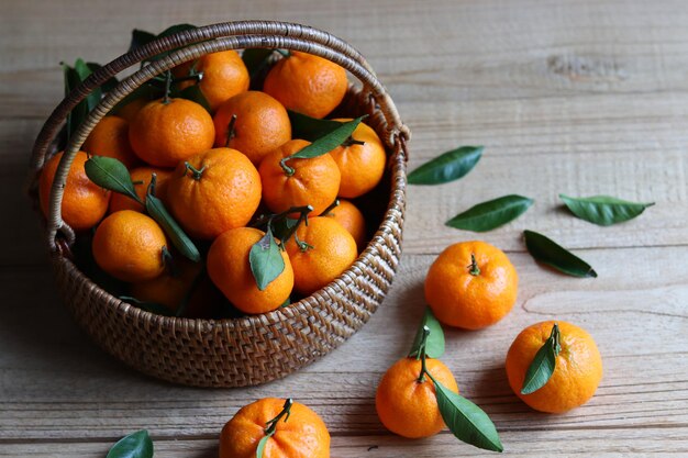 Foto grupo de frutas frescas de mandarina con hojas en la cesta de mimbre sobre la mesa de madera