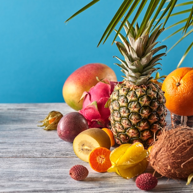 Foto grupo de frutas tropicales exóticas. mango, fruta del dragón, maracuyá, coco, piña, carambola, kumquat sobre un fondo azul con espacio de copia. concepto saludable vegetariano.