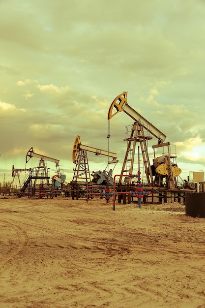 Grupo de gatos de bomba de aceite y cabezal de pozo con inducido de válvula durante la puesta de sol en el campo petrolífero. Concepto de petróleo y gas. Fondo espectacular cielo nublado. Tonificado.