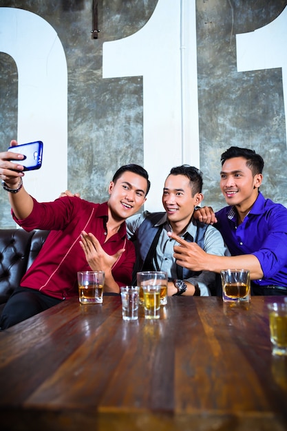 Grupo de gente de fiesta asiática de jóvenes amigos tomando fotos o selfies con su teléfono móvil o celular en un elegante club nocturno