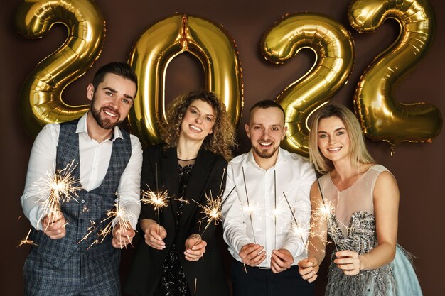 Grupo de gente hermosa fiesta bien vestida que celebra el año nuevo 2022 con bengalas encendidas