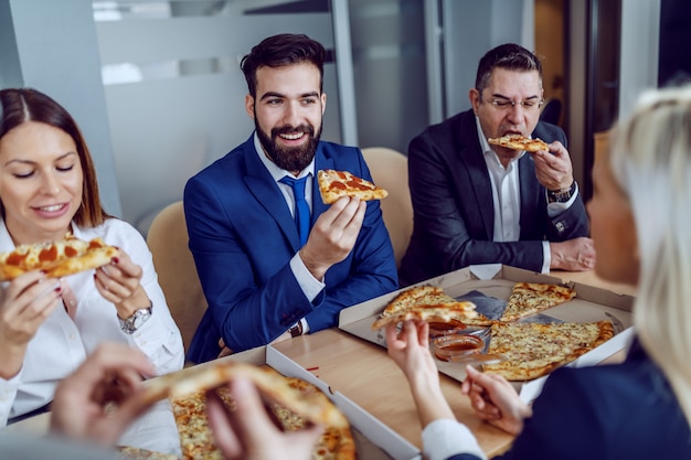 Grupo de gente de negocios hambrientos con pizza para el almuerzo mientras está sentado en la sala de juntas.