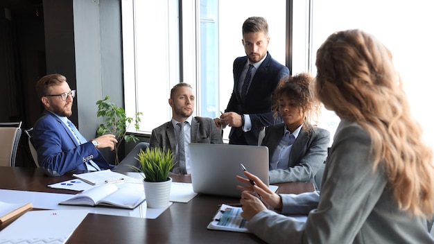 Grupo de gente de negocios moderna en ropa formal discutiendo negocios y sonriendo mientras está sentado en la oficina.