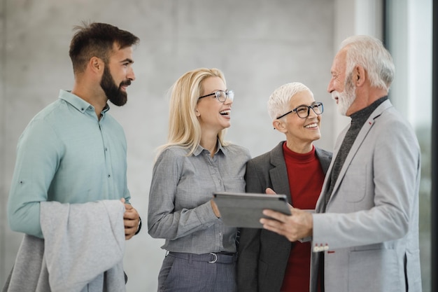 Un grupo de gente de negocios sonriente usando una tableta digital y discutiendo entre ellos durante la reunión en la oficina moderna.