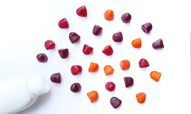 Grupo de gomitas multivitamínicas rojas, naranjas y púrpuras con la botella aislada sobre fondo blanco. Concepto de estilo de vida saludable.