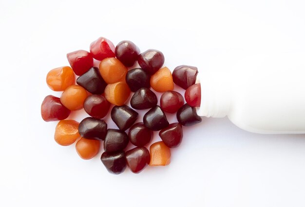 Grupo de gomitas multivitamínicas rojas, naranjas y púrpuras con el frasco aislado sobre fondo blanco.