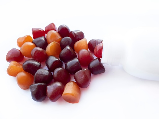 Grupo de gomitas multivitamínicas rojas, naranjas y púrpuras con el frasco aislado sobre fondo blanco.