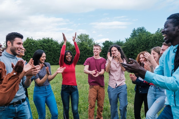 Grupo heterogêneo de jovens de diversas origens batendo palmas juntos ao ar livre Conceito Integração estilo de vida amizade