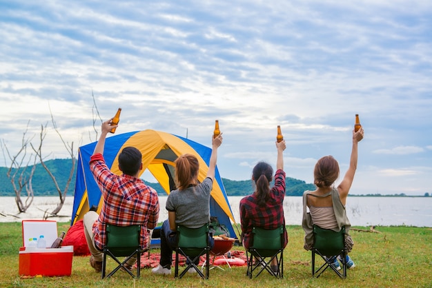 Foto grupo de hombre y mujer disfrutar de campamento de picnic y barbacoa en el lago con tiendas de campaña en el fondo. joven mujer de raza mixta asiática y el hombre.