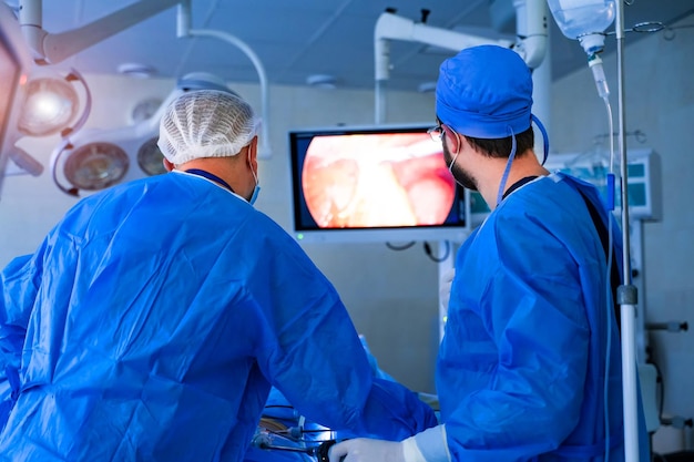 Grupo de hombres cirujanos que trabajan con equipos modernos Vista posterior del equipo de especialistas en ropa médica especial mirando el monitor en la sala de operaciones