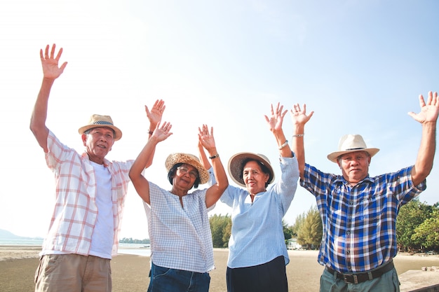 El grupo de hombres y mujeres de edad avanzada en Asia visitó el mar. Levanta ambos brazos con placer.