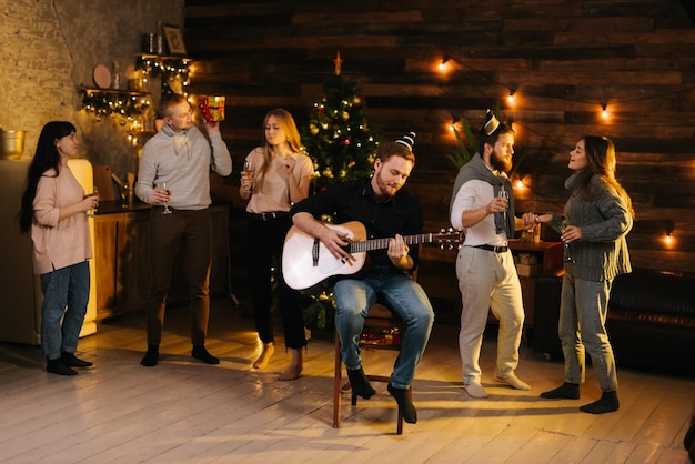 Grupo de hombres y mujeres jóvenes canta en una fiesta de Navidad en una casa acogedora