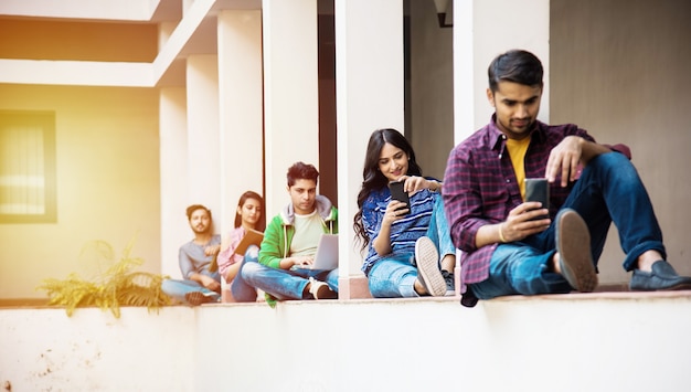 Grupo indiano asiático de estudantes universitários usando smartphones para redes sociais, enviando mensagens de texto, assistindo a vídeos