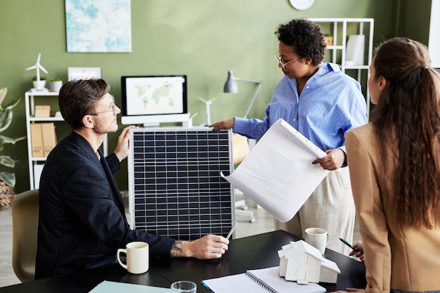 Grupo de ingenieros que trabajan con panel solar en equipo que discuten y planifican trabajos alternativos