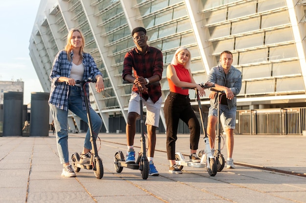 Grupo interracial de amigos montan scooters eléctricos en la ciudad