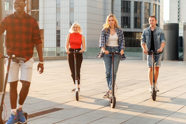 Grupo interracial de amigos montan scooters eléctricos en la ciudad