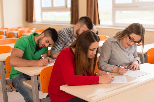 Grupo jovem de estudantes adolescentes atraentes em uma sala de aula da faculdade, sentados em uma mesa, aprendendo lições