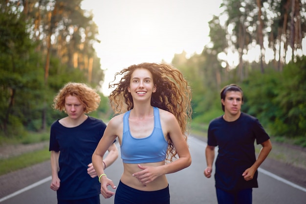Grupo jovem homem e mulher caucasiano correndo estrada de asfalto manhã ensolarada de verão