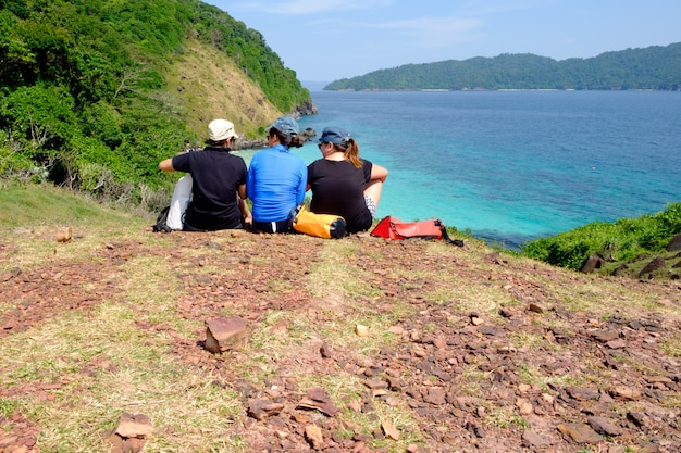 Grupo jovem, menina, sentar-se, penhasco, montanhas, mar, paisagem, azul, céu