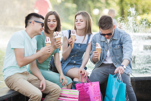 Grupo de jóvenes alegres comiendo helado y divirtiéndose. Compradores al aire libre. Gente después de comprar. Divertido grupo de amigos descansando cerca de la fuente.