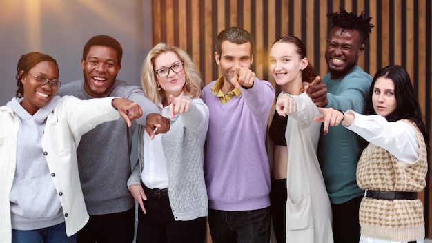 Foto grupo de jóvenes alegres parados uno cerca del otro y señalándote