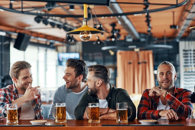 Grupo de jóvenes alegres en ropa casual disfrutando de la cerveza y comunicándose