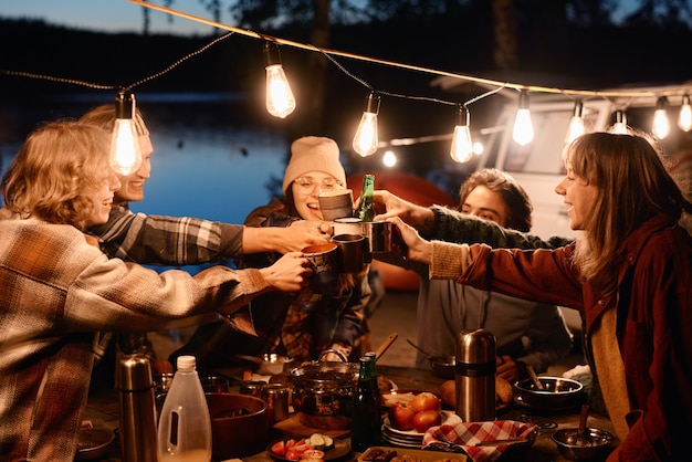 Grupo de jóvenes amigos brindando con bebidas y divirtiéndose durante un picnic en la naturaleza