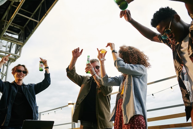 Grupo de jóvenes amigos extasiados bailando en la fiesta de la azotea en un café al aire libre