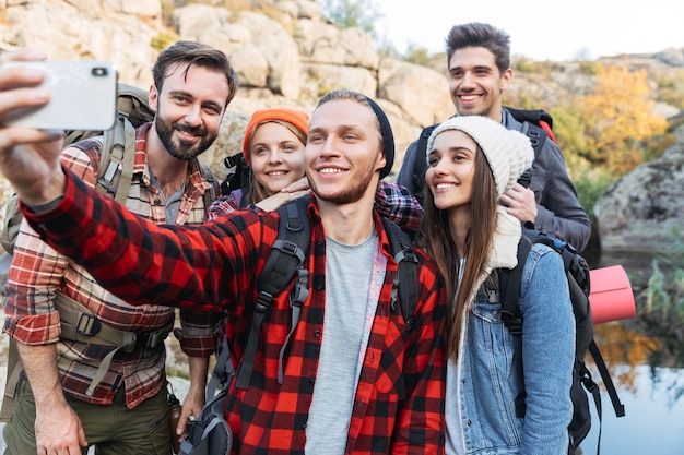 Grupo de jóvenes amigos felices llevando mochilas en una caminata juntos, tomando un selfie