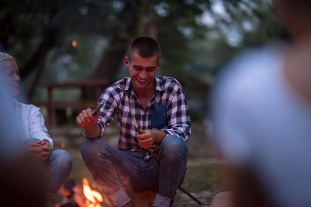 Foto un grupo de jóvenes amigos felices relajándose y disfrutando de la noche de verano alrededor de una fogata en la orilla del río