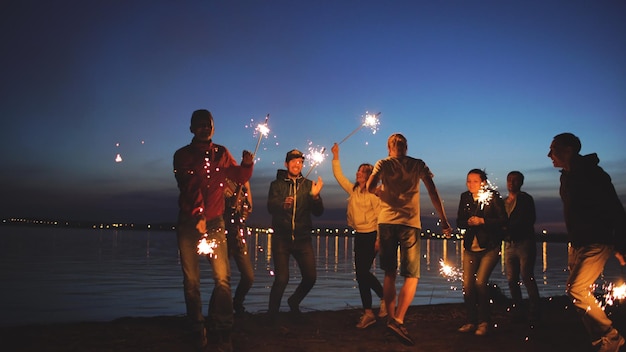 Grupo de jóvenes amigos haciendo una fiesta en la playa Amigos bailando y celebrando con bengalas