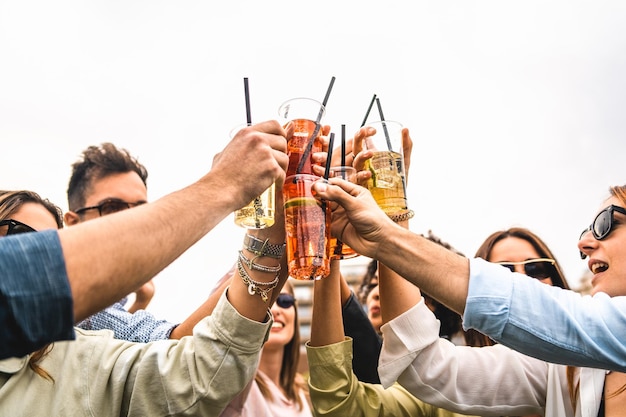 Grupo de jóvenes amigos levanta vasos de plástico con spritz y cócteles de frutas para celebrar un brindis contra un cielo de fondo blanco concepto de gente feliz divirtiéndose al aire libre bebiendo y tintineando