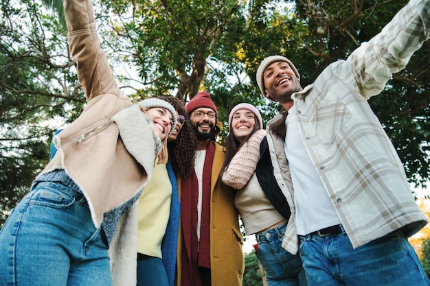 Un grupo de jóvenes amigos multirraciales divirtiéndose juntos en un parque haciendo actividades de fin de semana de otoño usando abrigos y sombreros Cinco personas felices sonriendo y caminando al aire libre Concepto de estilo de vida