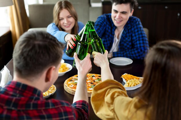 Grupo de jóvenes amigos con pizza y botellas de cerveza celebran en un café.