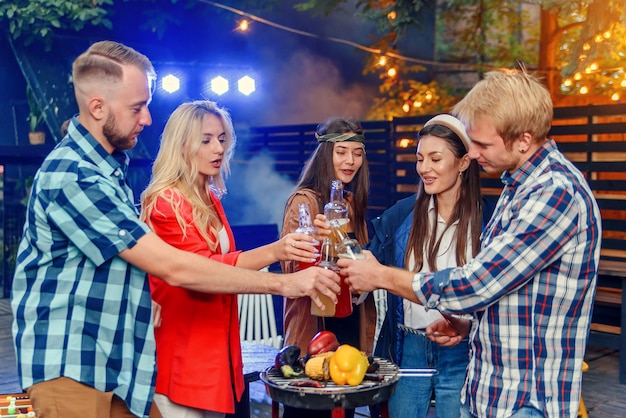 Grupo de jóvenes amigos que se divierten en una fiesta de verano junto a la piscina, beben cerveza e invitan a más amigos a unirse a ellos.