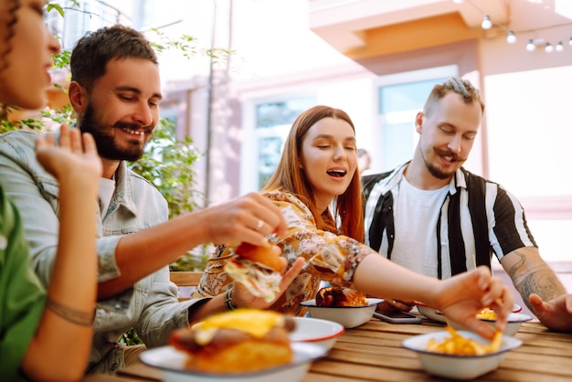 Foto grupo de jóvenes amigos reunidos en un café comiendo hamburguesas frescas y sabrosas comida rápida gente