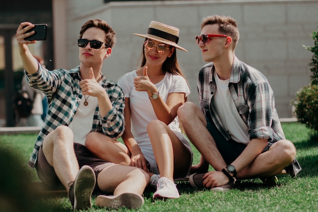 Un grupo de jóvenes amigos Selfies haciendo un pulgar hacia arriba en el Sunny Lawn