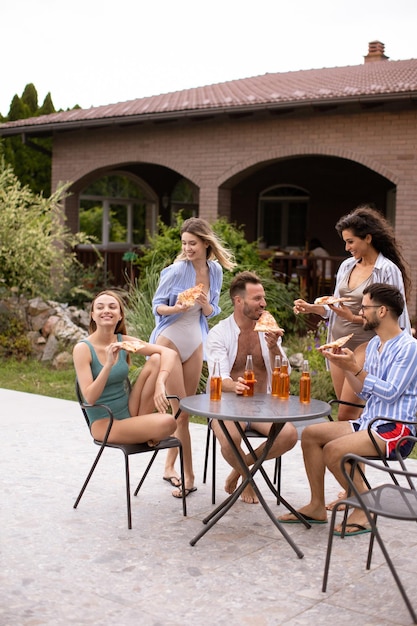 Grupo de jóvenes animando con sidra y comiendo pizza junto a la piscina en el jardín