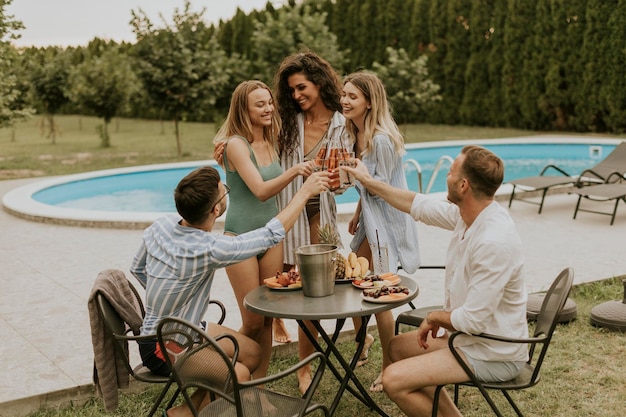 Grupo de jóvenes animando con sidra junto a la piscina en el jardín