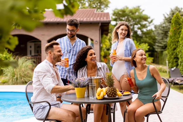 Grupo de jóvenes animando con sidra junto a la piscina en el jardín