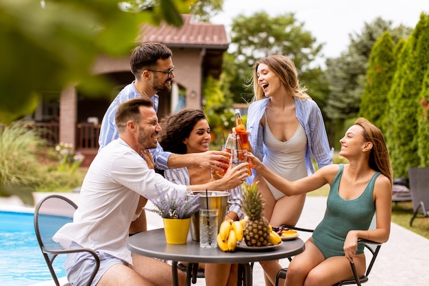 Grupo de jóvenes animando con sidra junto a la piscina en el jardín