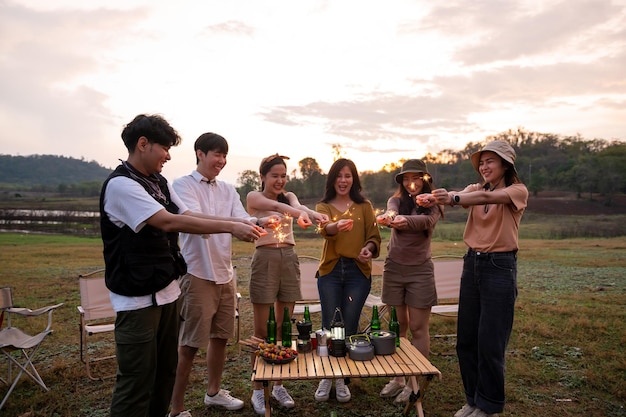 Grupo de jóvenes asiáticos disfrutan acampando jugando bengalas en un campamento natural al atardecer