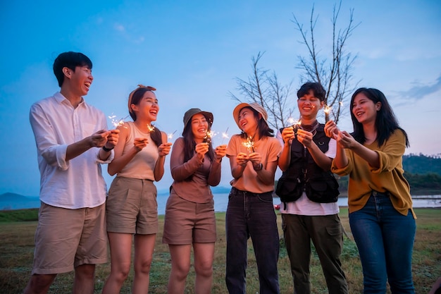 Grupo de jóvenes asiáticos disfrutan acampando jugando bengalas en un campamento natural al atardecer