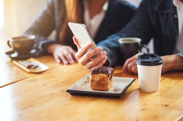 Un grupo de jóvenes asiáticos que usan y miran el mismo teléfono móvil juntos en la cafetería